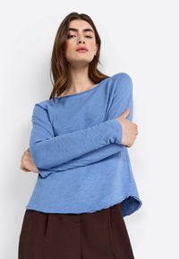 Light blue, long-sleeve top in a relaxed fit with a scoop neckline and unfinished hem. Made of soft fabric, featuring a smooth texture.