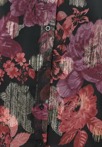 Schwarze Bluse mit großen roten und lila Blumenmustern, versehen mit metallischen Akzenten und schwarzen Knöpfen an der Vorderseite. Weicher, leichter Stoff.