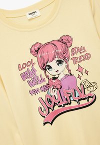 Żółta bawełniana bluza z grafiką postaci o różowych włosach trzymającej lody, z dodatkowymi, zabawnymi tekstami oraz ilustracjami kości.