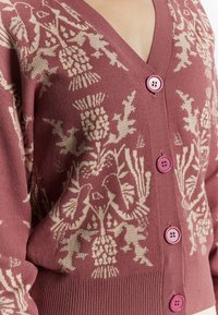Cardigan lavorato a maglia in rosa e crema, con scollatura a V, motivo floreale decorativo e bottoni rosa. Texture morbida con polsini a costine.
