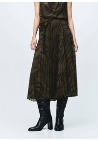 Falda marrón con pliegues y un diseño texturizado, acompañada de unas botas de cuero negro hasta la rodilla con tacón cuadrado.
