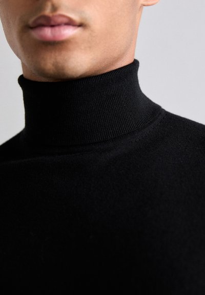 Svart polotröja i närbild, med ribbat mönster och figurnära design, som framhäver det släta tyget och den höga kragen.