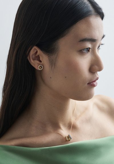 Zlatne naušnice s cvjetnim uzorkom i prozirnim kamenčićima; delikatna zlatna ogrlica sa privjeskom koji ima plave kamenčiće.