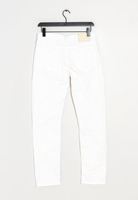 Jean en denim blanc suspendu sur un cintre noir, montré de l'arrière avec des poches et des passants de ceinture visibles, sur fond blanc.