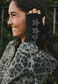 Černé bezprsté rukavice se stříbrnými hvězdnými ozdobami na horní straně; nošeny s bundou s leopardím potiskem.