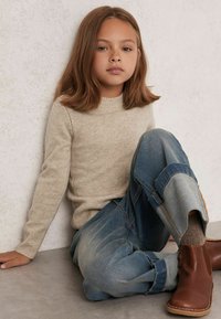 Maglione lavorato a maglia color beige chiaro con orlo a costine; jeans blu larghi con pannello in denim a contrasto; stivali alla caviglia in pelle marrone.