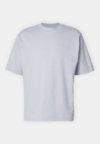 Camiseta de algodón de color azul claro y manga corta. Presenta un escote redondo y un logo bordado en el pecho. Textura suave y corte relajado.