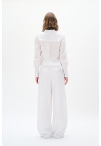 Weißes Hemd mit Rüschensaum und Puffärmeln, kombiniert mit weiten weißen Hosen, beide aus leichtem Stoff. Minimalistisches Design.