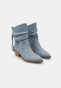 Botines de ante azul claro con un diseño arrugado, puntera afilada y tachuelas decorativas. Presentan un tacón de madera y un detalle de lazo en la parte trasera.
