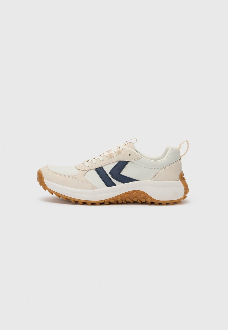 Chaussure de sport beige clair avec des accents bleu marine, upper en tissu texturé et une semelle en caoutchouc dotée de crampons ronds pour plus d'adhérence.