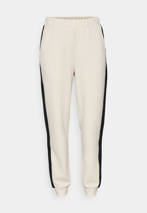 Béžové tepláky s čiernymi bočnými pruhmi, elastický pás a zúžené členky. Vyrobené z mäkkého a pružného materiálu, vybavené bočnými vreckami.