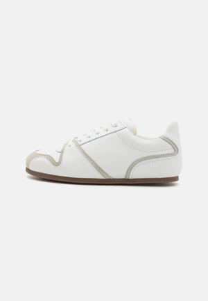 White sneaker with suede accents; features a rounded toe, flat sole, and six eyelets. Clean design with subtle stitching detail.