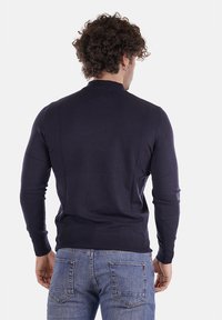 Maglione a maglia blu navy con maniche lunghe, polsini e orlo a coste. Il tessuto appare liscio e aderente, visto da dietro. Abbinato a jeans chiari.