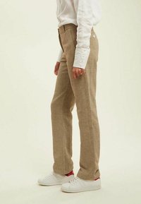 Pantalons à carreaux marron avec une coupe à jambe droite, taille haute, tissu texturé et poches latérales. Associés à des baskets blanches.