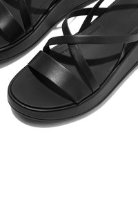 Zwarte leren sandalen met gekruiste banden, een gladde textuur en een brede zool, ontworpen voor comfort en stabiliteit.