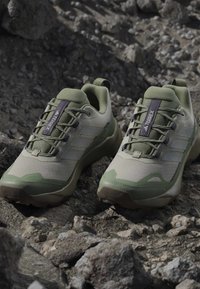 Paire de chaussures de randonnée Adidas Terrex vertes et beiges posées sur un sol rocheux en plein air.