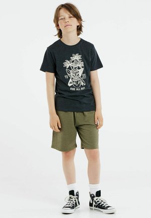 T-shirt grigia scura con grafica bianca di fiori e testo, abbinata a pantaloni corti verde oliva e sneakers alte nere con lacci bianchi.