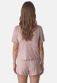 Set de pijama din satin roz deschis, format dintr-un top cu mânecă scurtă și șorturi. Textură moale, cu o croială lejeră și un design simplu. Fără modele vizibile sau accente.
