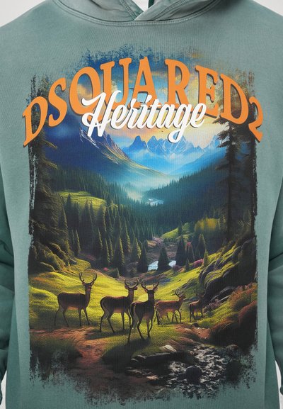 Zelena dukserica s kapuljačom koja prikazuje šareni pejzaž s planinama, rijekom i jelennima, uz narančasti natpis "DSQUARED2 Heritage."