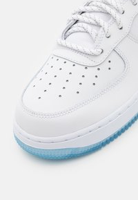 Sneaker bianco con punta perforata, tomaia in pelle liscia e suola traslucida blu chiaro. Presenta cuciture e lacci in contrasto.