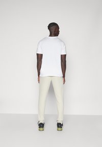 Hvid bomulds t-shirt parret med lysebeige joggers. Sorte og grønne sneakers med snørebånd. Enkelt og glat tekstur. Ingen synlige mønstre.