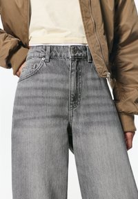 Jeans gri din denim cu picioare largi, cu o spălare estompată, dotate cu sistem de închidere cu nasture și fermoar, buzunare cusute și un material texturat.