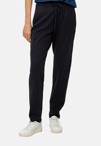 Donkerblauwe, lichte sweatpants met een elastische tailleband en trekkoord. Heeft zijzakken en een taps toelopend beenontwerp. G gedragen met witte sneakers.