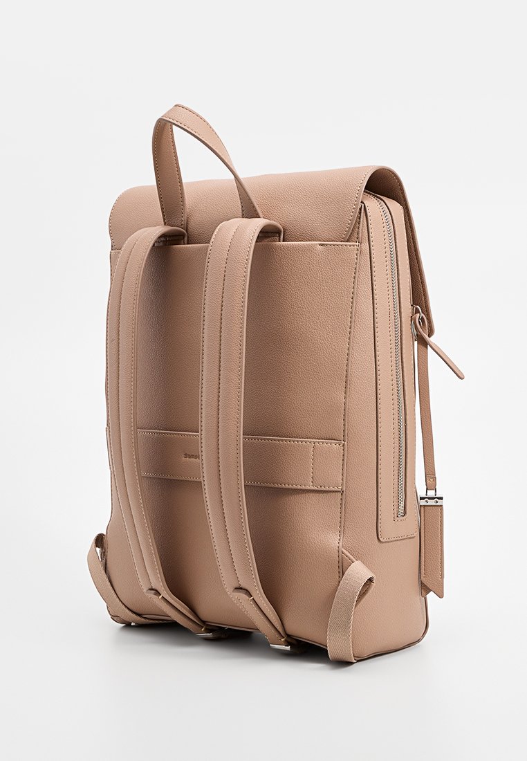Beige Leder-Rucksack mit verstellbaren Trägern, rechteckiger Form, Klappe oben und einer seitlichen Reißverschlusstasche. Texturierte Oberfläche mit genähten Akzenten.