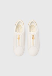 Baskets blanches avec fermeture éclair à l'avant, garnitures en métal doré et dessus en tissu texturé. Le design comprend un accent discret beige au talon.