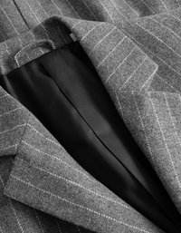 Γκρι σακάκι από μάλλινο ύφασμα με λευκές ρίγες, με μαύρη επένδυση ορατή στο εσωτερικό. Ραμμένα πέτα και υφή υφάσματος.