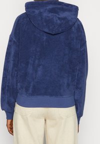 Granatowy hoodie z kapturem o miękkim, teksturowanym wykończeniu. Posiada ryflowany dół i mankiety, luźny krój oraz casualowy design.