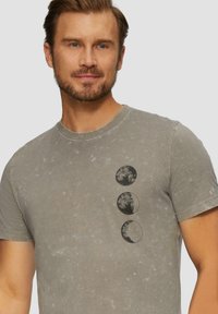 Grijze katoenen t-shirt met een ronde maanfaasafbeelding in zwart op de voorkant. De stof heeft een gestructureerd, versleten uiterlijk.