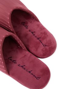 Pluszowe, bordowe kapcie z żeberkowaną zewnętrzną powierzchnią, otwartym fasonem i miękkim wnętrzem, z haftowanym napisem na wkładce.