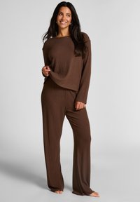 Bruin geribd loungewear set bestaande uit een top met lange mouwen en brede halslijn, evenals een broek met een losse pasvorm. Zacht, gestructureerd materiaal.