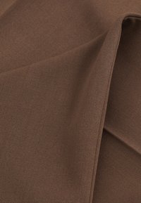 Tejido marrón texturizado doblado con patrón visible de tejido diagonal y sombras suaves que acentúan los pliegues y dobleces.