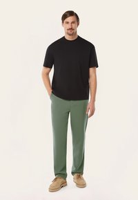 Zwart T-shirt met korte mouwen, gecombineerd met groene broeken en beige schoenen. Eenvoudig ontwerp, gladde textuur en een relaxte pasvorm.