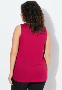 Fuchsia ärmelloses Top aus weichem Baumwollmix, mit glatter Textur und langer Form, kombiniert mit schwarzen strukturierten Hosen.