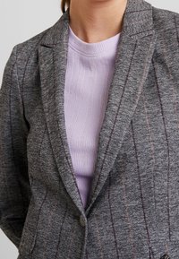 Grå blazer med ljuslila randig accent, med en snedkrage, enknappsstängning och textilstruktur.