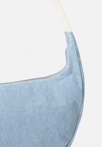 Borsa in denim blu chiaro con una forma curva, dotata di una tracolla crema e dettagli in zip argentati. Striature verticali sottili nel tessuto.