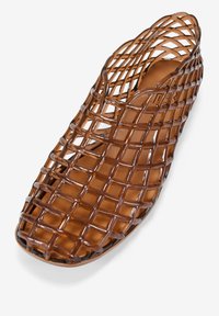 Zapato marrón de malla abierta sin cordones con un patrón tejido, hecho de material flexible, que presenta una punta redondeada y un revestimiento interior suave.