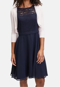 Vestido azul marino con corsé de encaje, falda acampanada y un cárdigan crema de mangas tres cuartos. Textura suave y diseño elegante.