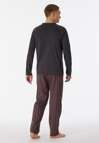 Herren Loungewear-Set mit einem dunkelgrauen Langarmshirt und gestreiften Pants in Rot, Grau und Weiß. Weicher Stoff mit lockerer Passform.