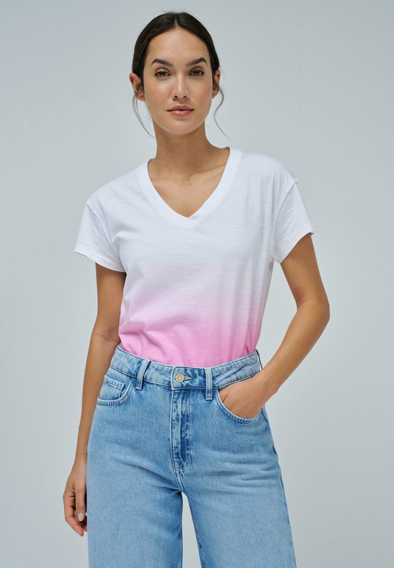 Camiseta de algodón blanca con un degradado ombré rosa, diseño de escote en V y mangas cortas, combinada con unos vaqueros de mezclilla de tiro alto en azul claro.
