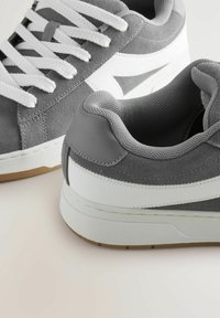 Sneakers bas gris et blanc avec des lacets blancs et une semelle en gomme, présentant un mélange de matériaux en daim et en cuir.