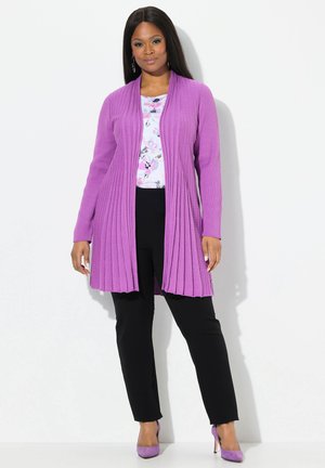Hellblauer, gerippter Cardigan mit langen Ärmeln, offenem Vorderteil, getragen über einem floral bedruckten Oberteil und schwarzen Hosen. Akzent durch passende lila Schuhe.