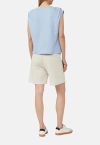Top in cotone azzurro chiaro con maniche a sbuffo, abbinato a pantaloni corti crema. Il modello indossa sneakers bianche con accenti neri e suole marrone chiaro.