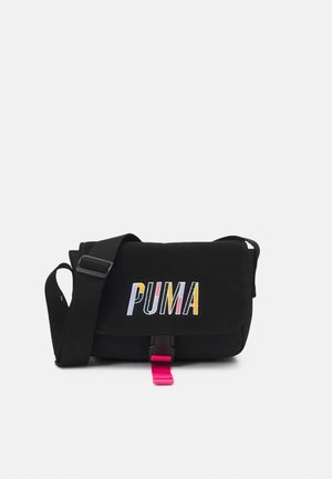 Czarna torba na ramię z regulowanym paskiem, klapka z zamknięciem z kolorowym napisem "PUMA" i różową zawieszką przy klamrze.