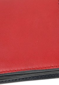 Gros plan du bord d'un portefeuille en cuir rouge avec des coutures visibles et une doublure intérieure noire.