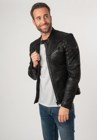 Zwarte leren motorjack met een gestructureerde afwerking, voorzien van ritsen en drukkers, gecombineerd met een eenvoudig wit T-shirt en blauwe spijkerbroek.