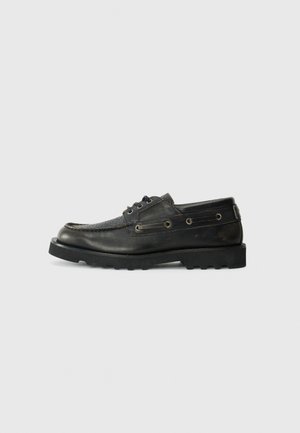 Black leather boat shoe with textured vamp, round toe, two eyelets, and a rugged rubber outsole. Simple design with stitching details.